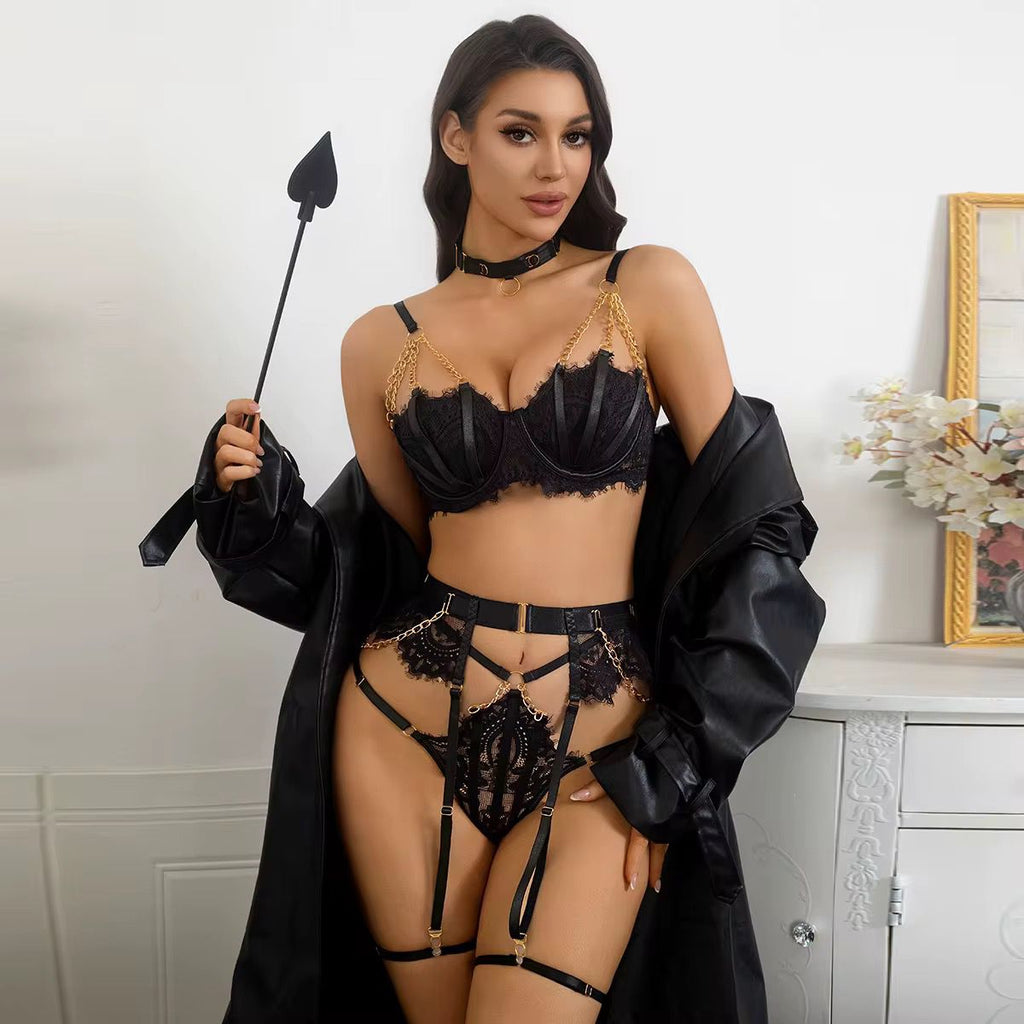 Woman in black lingerie holding a whip in a room with a white wall and decorative elements.